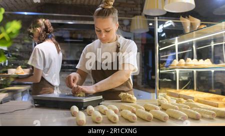 a chef girl cooks sausages in dough in an open kitchen in a cafe or restaurant. Stock Photo