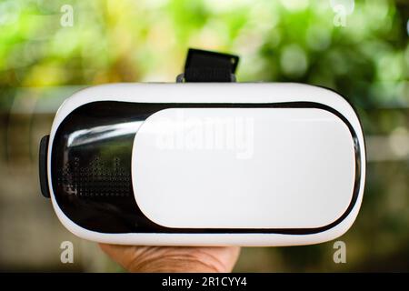 Male hand holding Virtual reality (VR) white and black. Man VR plays alone. Closeup, Blurred background. Stock Photo