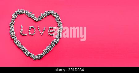 The heart symbol and the letter LOVE in the heart are made of small stones or pebbles placed on a red background. It is a concept of the day of love o Stock Photo