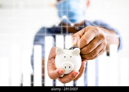 Businessman holding a white pig piggy bank and collecting coins in the piggy bank. Concept of men wearing a face mask to collect money during coronavi Stock Photo