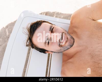 Young man lies on a sun lounger on the beach in the shade Stock Photo