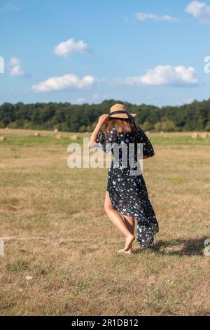 Young lady wearing dress and straw hat walking in marina. Greece, Hydra ...