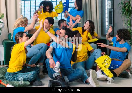 YES. Multiethnic sports fans laughing,  giving five, screaming and fist pumping celebrating favorite soccer team scoring goal. Happy people drinking j Stock Photo