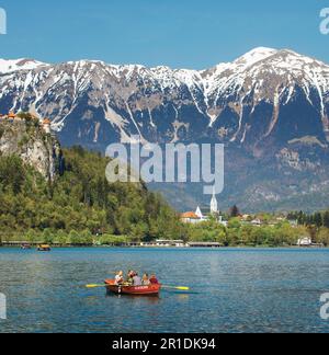 Bled, Upper Carniola, Slovenia.  Visitors enjoying a rowing excursion on Lake Bled.  The town and the snow covered Julian Alps in background. Stock Photo