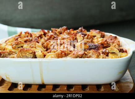 Closeup of Freshly Baked Banana Walnut Bread Pudding in Ceramic Bowl on a Wooden Breadboard Stock Photo