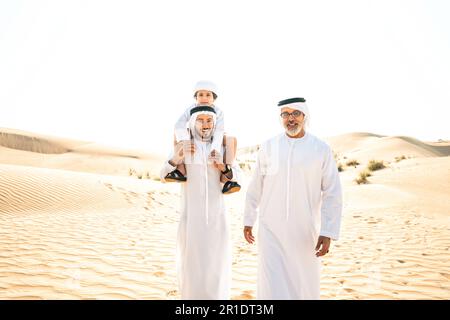 Three generation family making a safari in the desert of Dubai wearing white kandura outfit. Grandfather, son and grandson spending time together in t Stock Photo