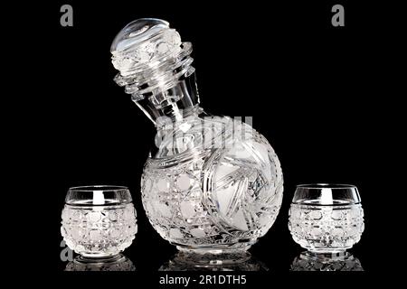 One crystal decanter and two glasses, macro, isolated on black background. Stock Photo