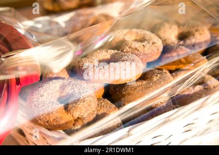 Homemade round biscuits ciambelli with sugar on top packed in white basket with transparent polyethylene film above. Selling sweets in the market Stock Photo