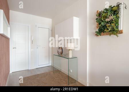 Simple but cozy entrance hall in light colors with an intercom, a glass console and a hanging cabinet with a stylish herbarium on the wall. The Stock Photo
