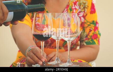 Hand poring red wine to wine glasses on table Stock Photo