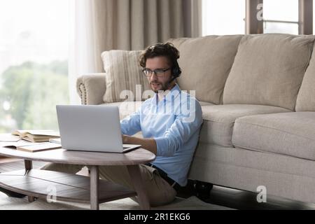 Focused positive student man in wireless headset using laptop Stock Photo