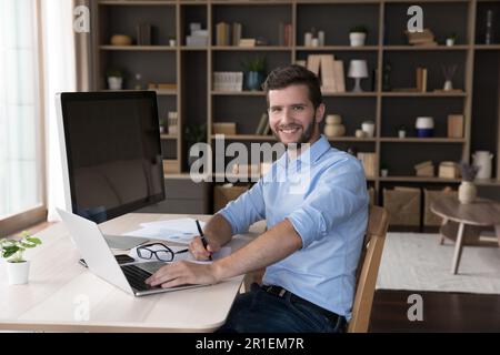 Happy freelance professional programmer sitting at table with workstation Stock Photo