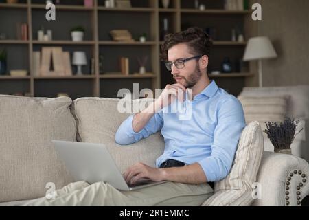 Serious pensive freelancer man in glasses relaxing on sofa Stock Photo