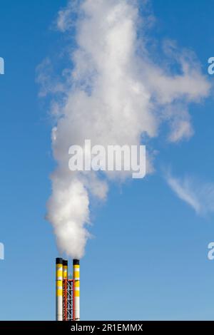 Chimney from a refuse incinerator emitting smoke and polluting the air against a clear blue sky. Stock Photo