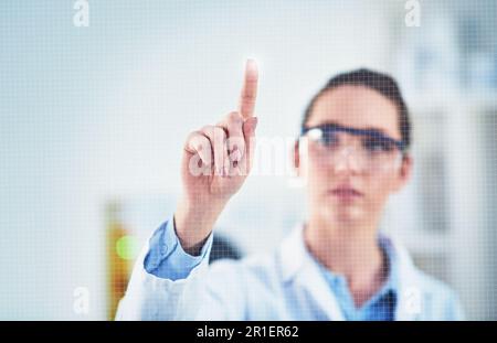 One bright idea coming up. a focused young female scientist wearing protective glasses while pointing with her finger on a glass wall. Stock Photo