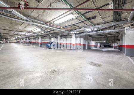 A few parking spaces of a large garage in an urban residential apartment building with white and red columns and boundaries Stock Photo