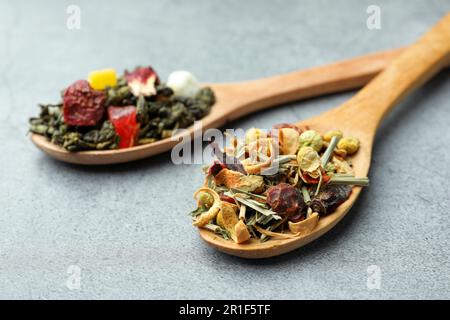 Different kinds of dry herbal tea in wooden spoons on light grey table, closeup Stock Photo