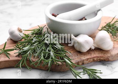 Sprigs of rosemary, mortar and garlic on white marble background, closeup Stock Photo