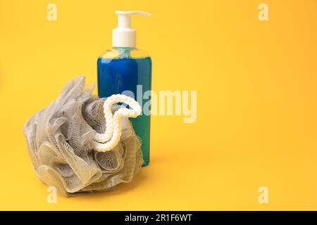 Grey shower puff and bottle of cosmetic product on yellow background, space for text Stock Photo