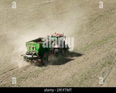 Modern tractor with trailer spreading fertilizer on field Stock Photo