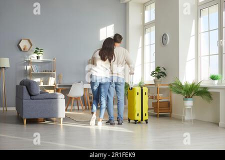 View from behind of hugging loving couple standing with suitcase at home Stock Photo