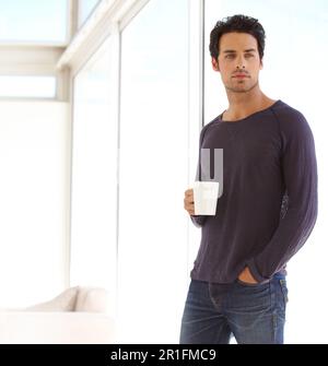 Handsome, casual and man with coffee standing by the window in a vacation house. Calm, relax and attractive male person drinking a mug of latte in the Stock Photo