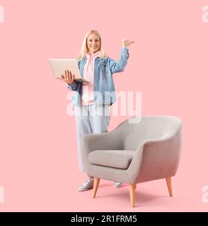 Mature female programmer with laptop pointing at something on pink background Stock Photo