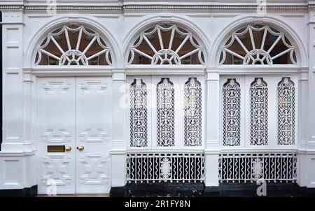 Front of building painted white, with fanlight windows and ornate grille Stock Photo