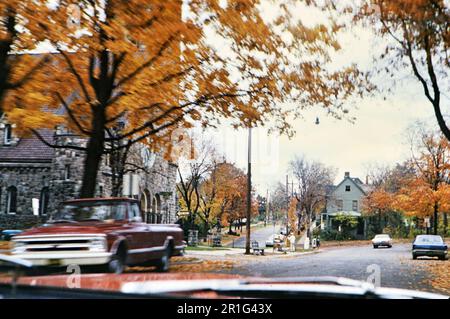 Car driving down a street, past a church, on an autumn day, people walking through their community ca. 1968 Stock Photo