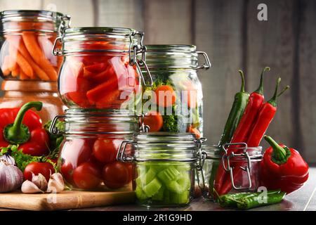 Jars with marinated food and raw vegetables on cutting board Stock Photo
