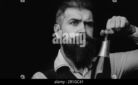 Portrait of a bearded waiter holding a champagne bottle. Close up portrait of man uncorking a bottle of champagne. Champagne wine. Man celebrating Stock Photo