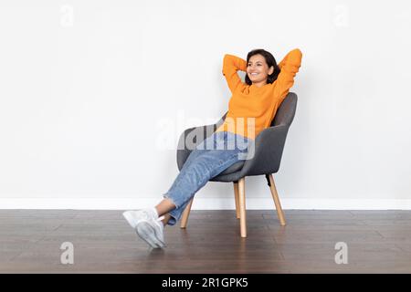 Positive young eastern woman relaxing in armchair at home Stock Photo