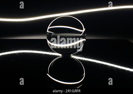 A glowing metallic sphere illuminated in the dark, with its reflection visible on the surface below Stock Photo