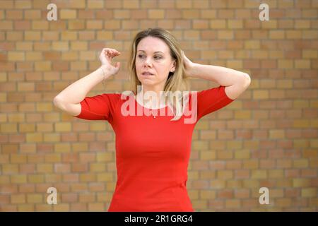 Critical attractive middle aged blonde woman in front of a wall stroking her Hair Stock Photo