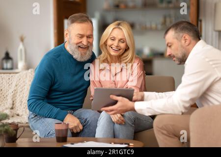 Professional Agent Showing Tablet To Excited Senior Couple At Home Stock Photo
