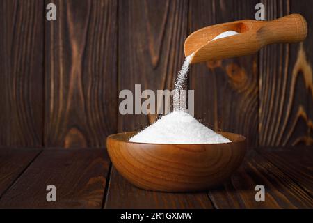 white sugar falling from scoop in bowl on table Stock Photo