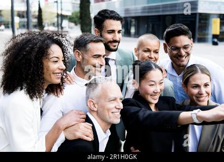 Multiracial group of successful business people taking a selfie outside. Diverse office colleagues taking a picture together smiling and bonding in Stock Photo