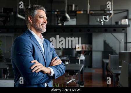 Happy successful mature business man standing in office arms crossed, side view. Stock Photo