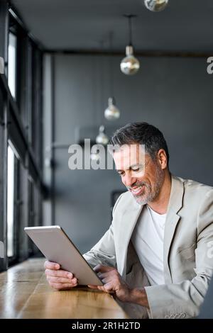 Mid aged business man using digital tablet computer sitting in modern office. Stock Photo