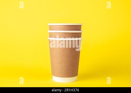 Three paper disposable cups on a yellow background isolated. Stock Photo