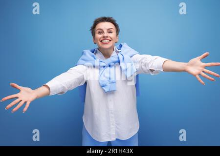 kind young dark-haired woman with sticking hair in a white shirt stretches out her arms for a hug Stock Photo
