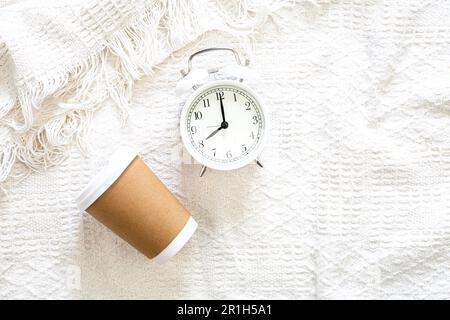 Paper cup and alarm clock in bed, top view. Stock Photo