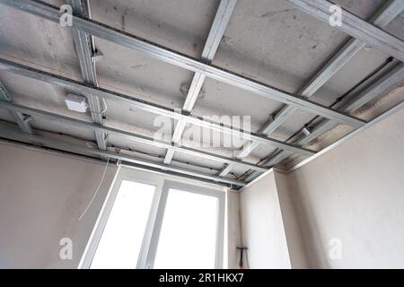 Installation of drywall. Workers are using screws and a screwdriver to attach plasterboard to the ceiling Stock Photo