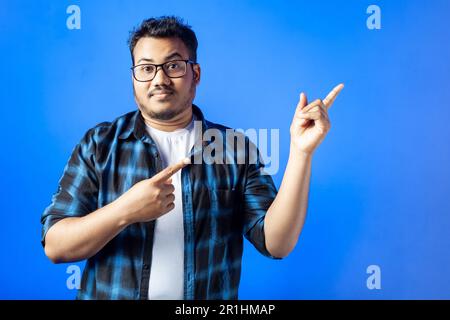 portrait of an Indian adult student pointing two fingers aside at empty space presenting something Stock Photo