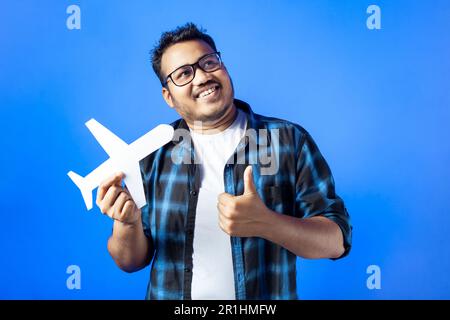 Indian ethnicity, toothy smile, journey. A young man smiling and showing thumb up hand, holding paper airplane craft Stock Photo