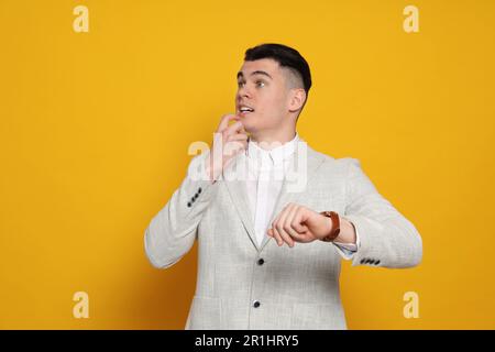 Emotional young man checking time on orange background. Being late concept Stock Photo