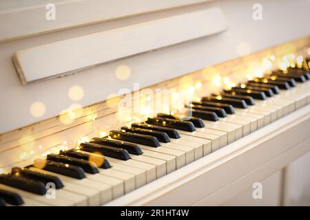 Glowing fairy lights on piano keys, closeup. Christmas music Stock Photo