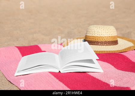 Open book, hat and striped towel on sandy beach Stock Photo