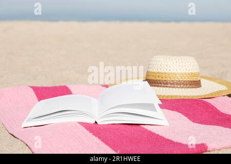 Open book, hat and striped towel on sandy beach near sea. Space for text Stock Photo