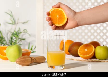 Woman squeezing orange over glass of juice at white wooden table, closeup Stock Photo